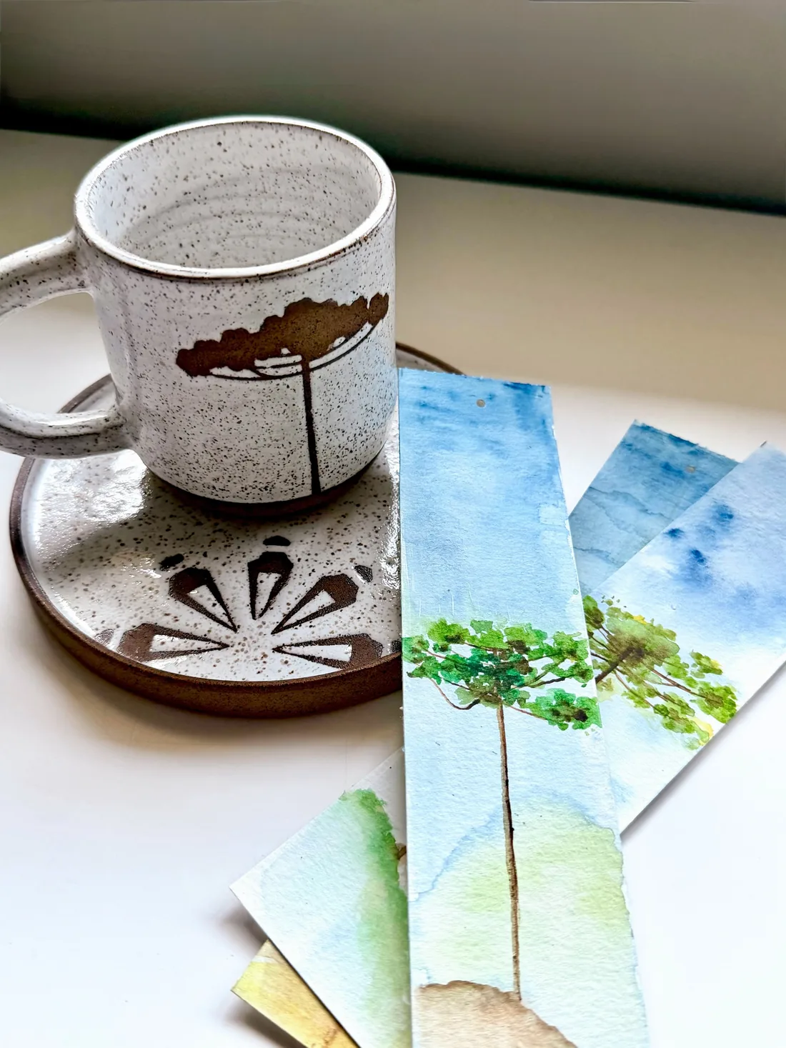 Caneca ao lado de marcadores de página pintados em aquarela.