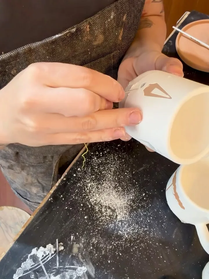 Caneca sendo acabada à mão na bancada do ateliê.