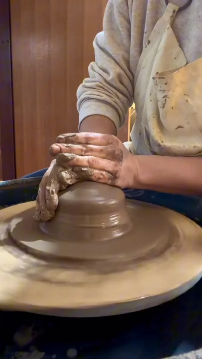 Mãos dando forma a uma peça de barro no torno.